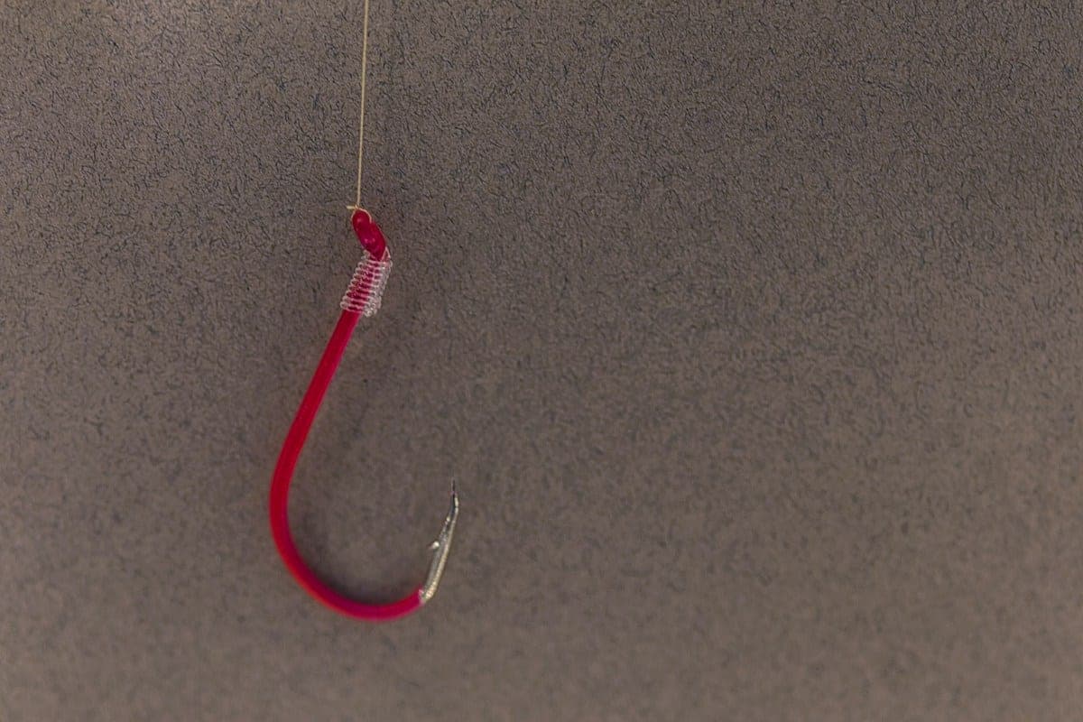 A red hook hanging from a line tied at its eye, with the wraps of the knot visible just below the eye