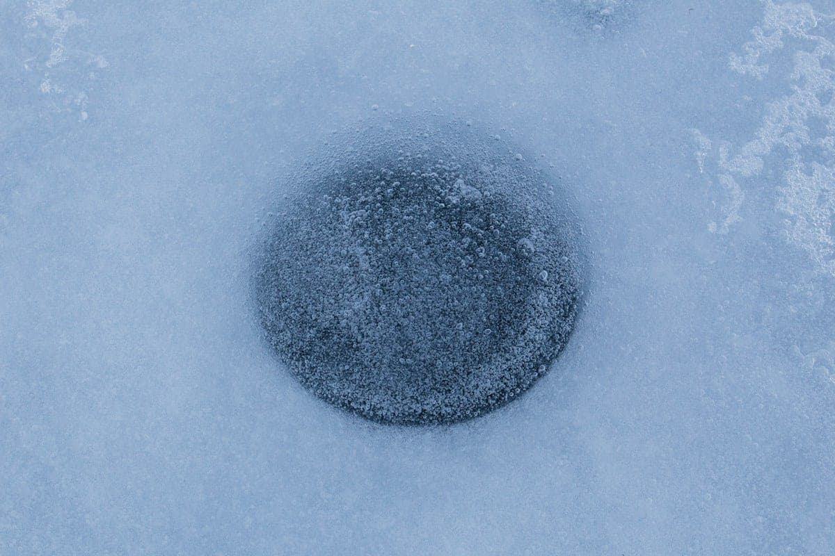A freshly drilled hole in the ice with an auger lying beside it