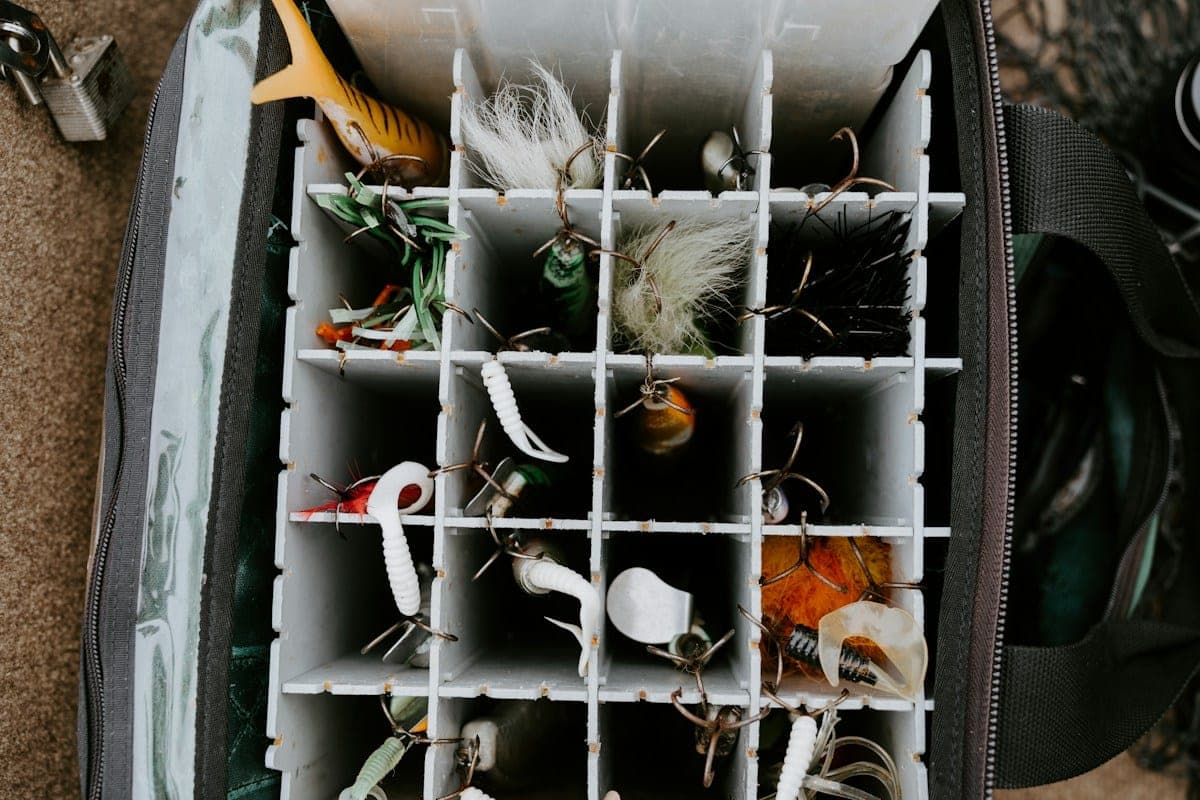 Looking down into an open tackle bag at a divided tray, with soft plastic baits and hooked lures in its compartments